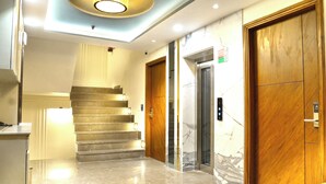 Un hall d’hôtel moderne avec un escalier en marbre, des portes en bois et un ascenseur.
