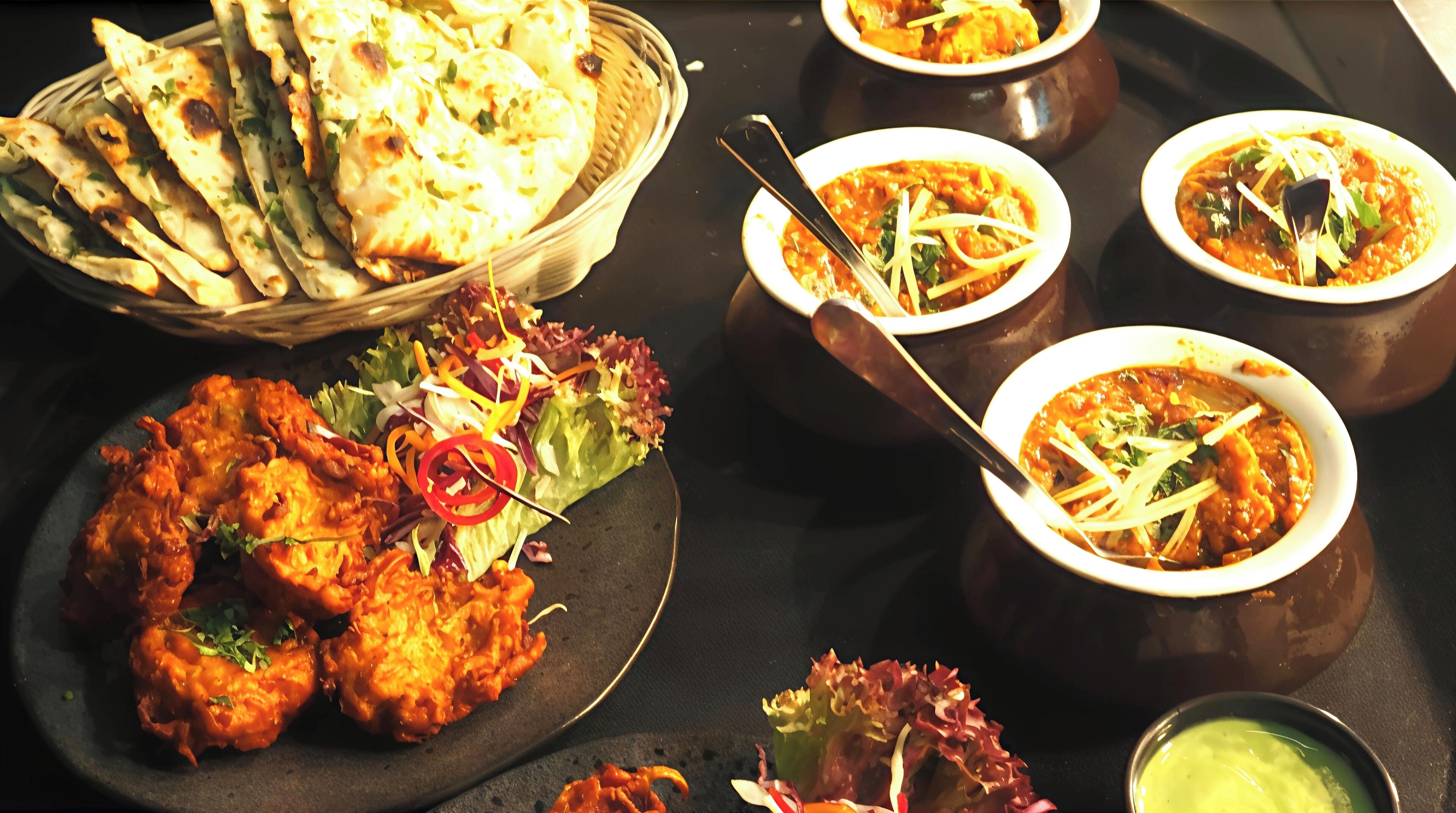 A table with various dishes including naan bread, curry, and a salad.