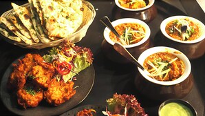 A table with various dishes including naan bread, curry, and a salad. - Hotel Mountain Bliss new delhi  (New Delhi)