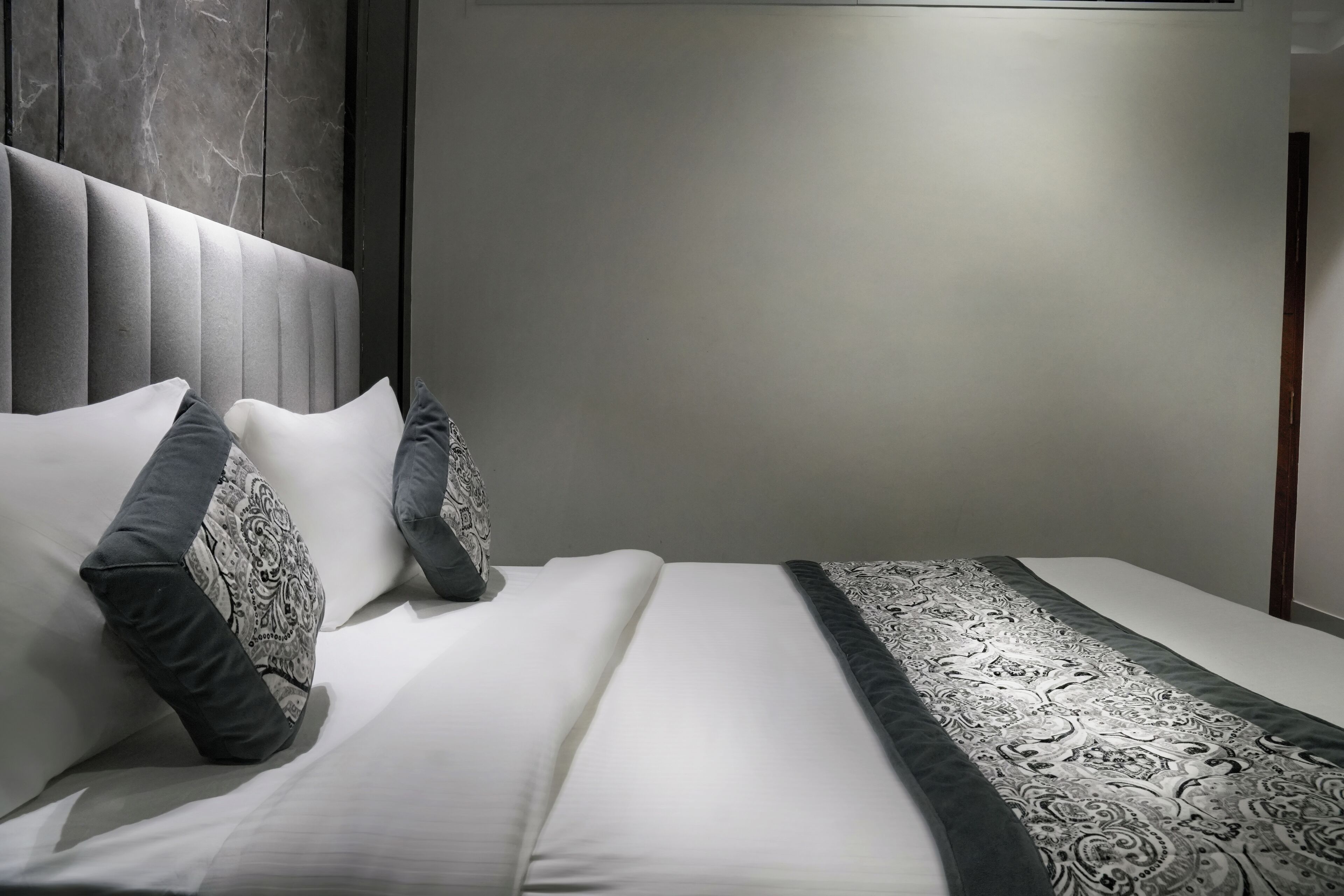 A modern hotel room with a large bed, a headboard with a marble-like texture, and a patterned throw blanket.