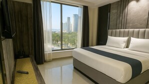 A modern hotel room with a large bed, a TV, and a view of tall buildings. - Hotel Mountain Bliss new delhi  (New Delhi)