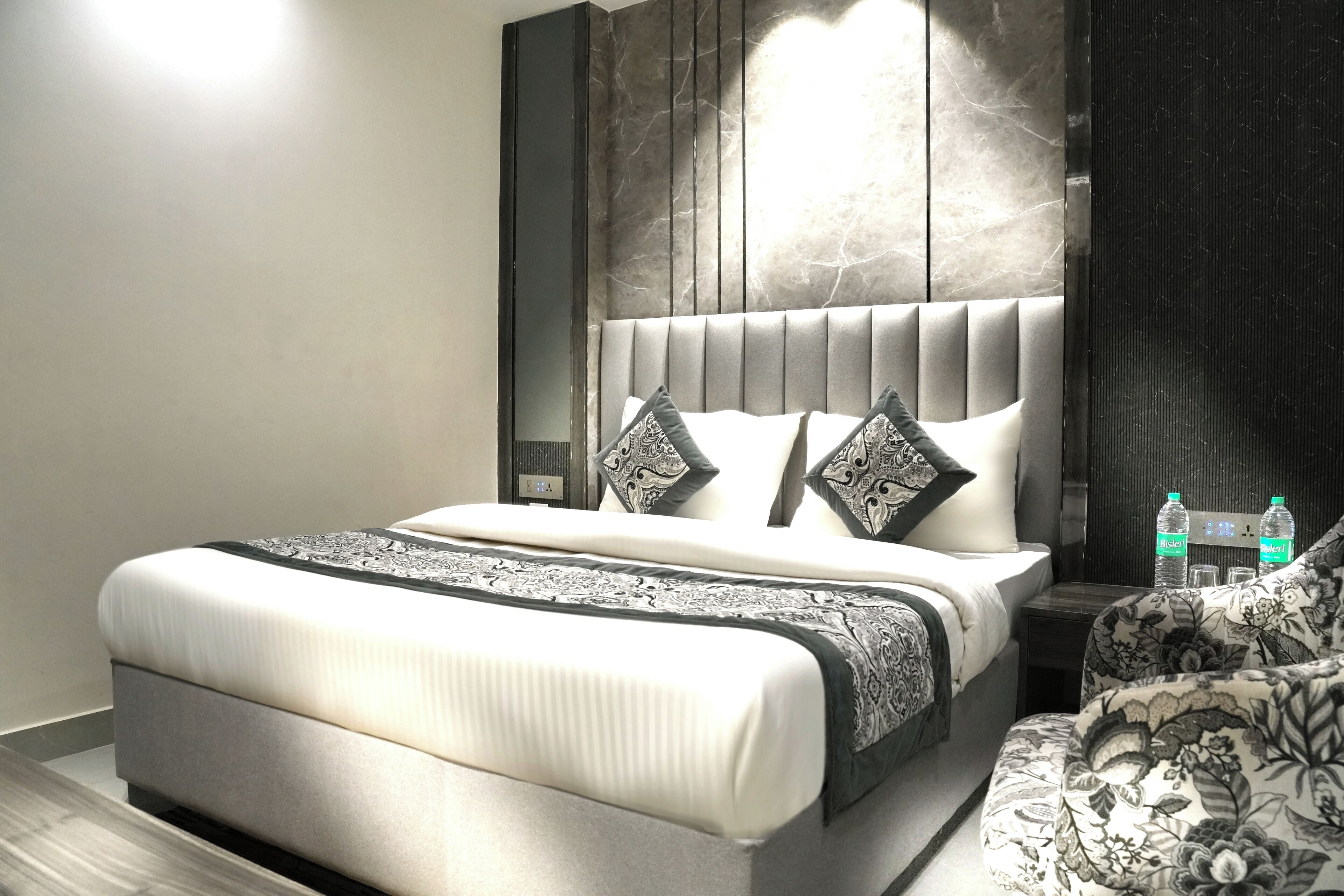 A modern bedroom with a large bed, a headboard with vertical lines, and a bedside table with two bottles of water.