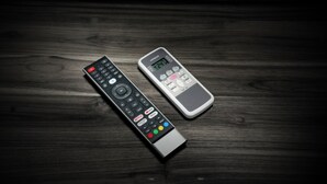 Two remote controls on a dark wooden surface. - Hotel Mountain Bliss new delhi  (New Delhi)
