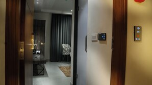 Un couloir d’hôtel avec une porte en bois, un écran numérique affichant le numéro de chambre 201, une chaise et un bureau avec une lampe.
