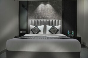 Een moderne hotelkamer met een groot bed, een hoofdbord met verticale lijnen, twee kussens met een patroon, een nachtkastje met waterflesjes, en een wand met een marmerachtige textuur.