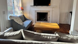 Una sala de estar acogedora con chimenea, un televisor montado encima, un sofá y una mesa de centro.