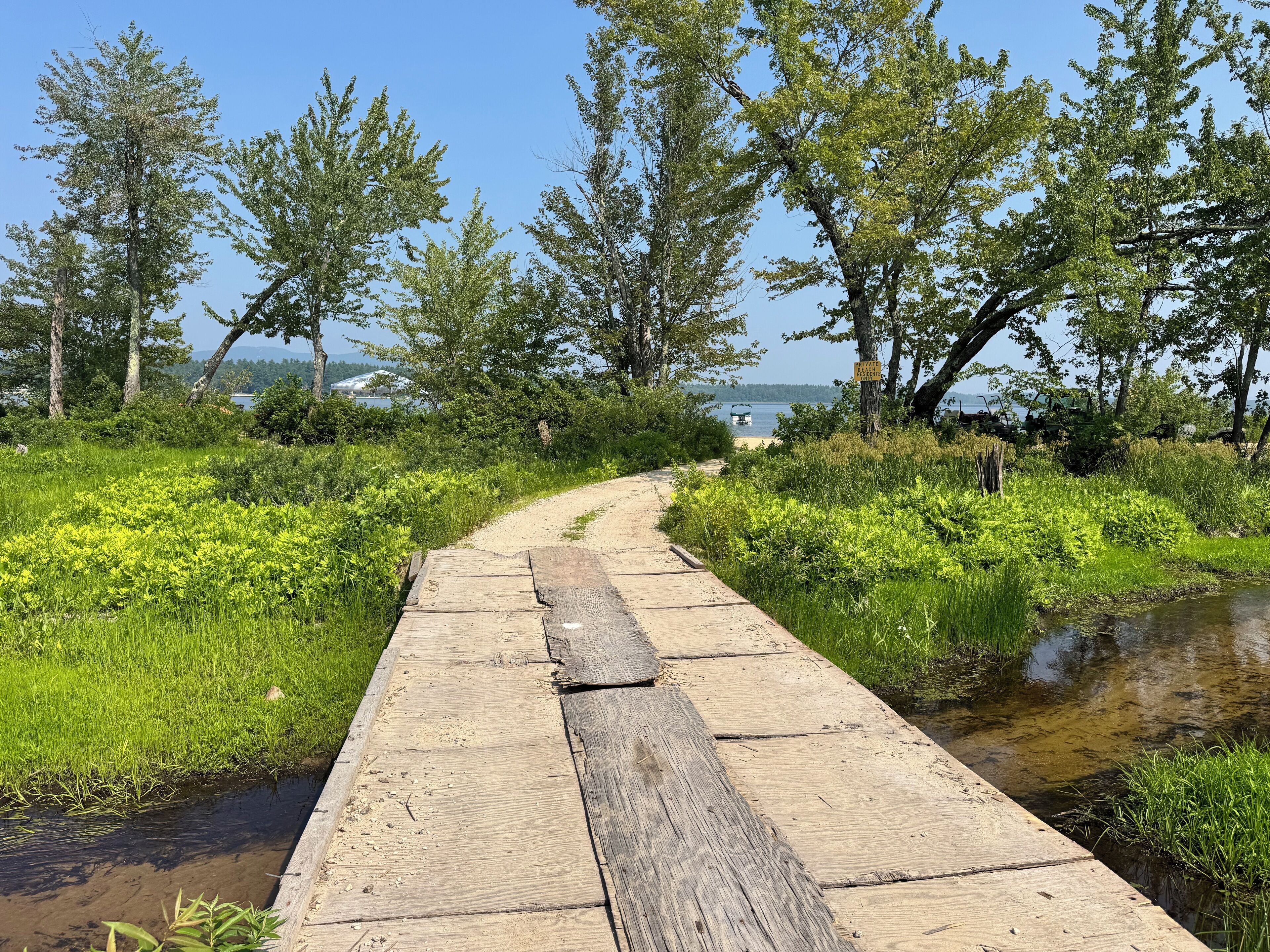 A wooden boardwalk leading to a body of water, surrounded by lush greenery and trees.