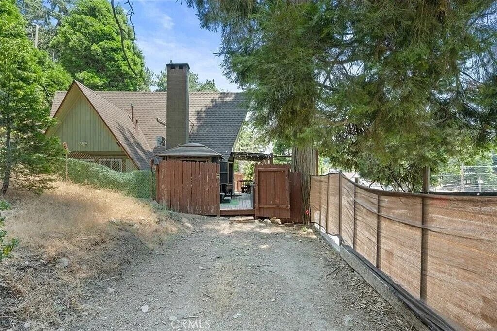 A rustic cabin with a chimney, a fenced yard, and a wooden deck.