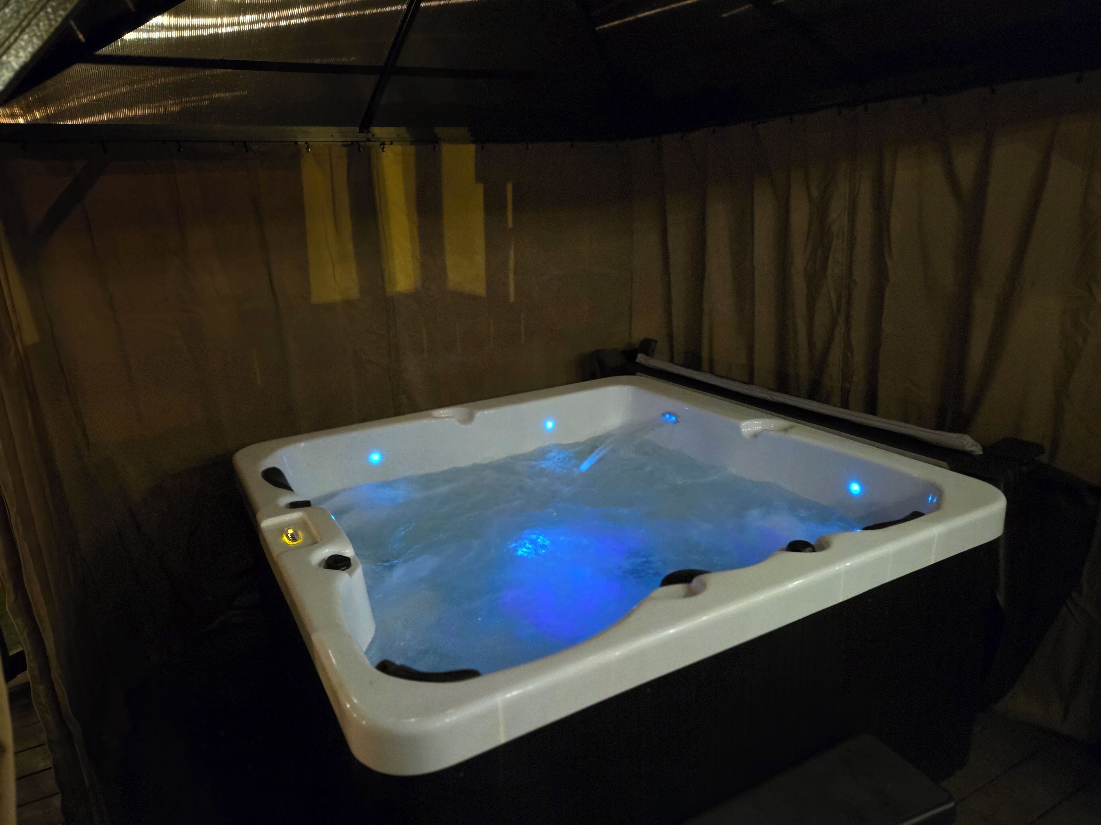 Ein Whirlpool mit blauen LED-Leuchten, umgeben von Vorhängen und einem Holzboden.