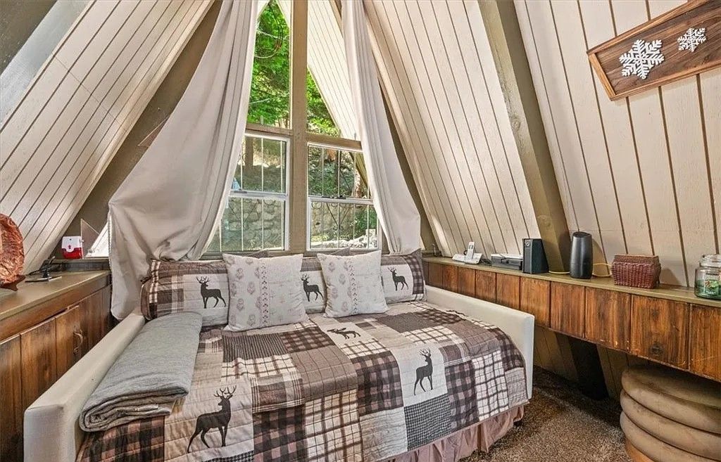 Un dormitorio acogedor con techo inclinado, una cama con colcha escocesa de estampado de ciervo y una ventana con cortinas.