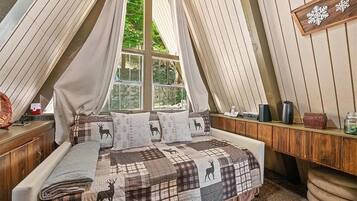 Un dormitorio acogedor con techo inclinado, una cama con colcha escocesa de estampado de ciervo y una ventana con cortinas.