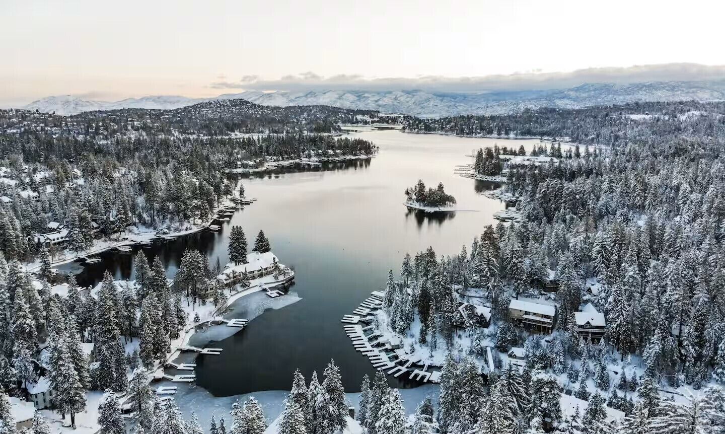 A snow-covered landscape with a lake, surrounded by dense forests and mountains.