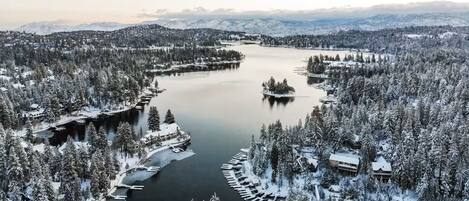 A snow-covered landscape with a lake, surrounded by dense forests and mountains.