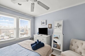 A bedroom with a bed, a TV on a dresser, a chair, and a ceiling fan.