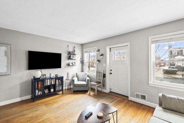 A living room with a flat-screen TV, a bookshelf, a grey armchair, a wooden coffee table, and a sofa.
