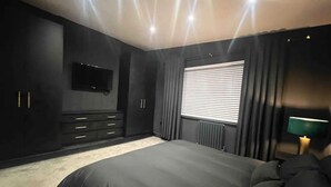 Ein modernes Schlafzimmer mit einem großen Bett, dunklen Wänden, einem Flachbildfernseher und einer Heizung.