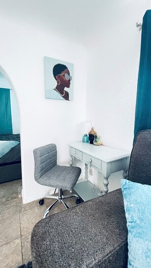 Ein Zimmer mit Schreibtisch, Stuhl, Bett und einem an der Wand hängenden Bild.