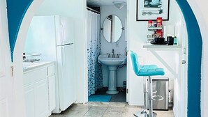 Um corredor estreito com um arco azul que dá para um banheiro com pia e espelho.