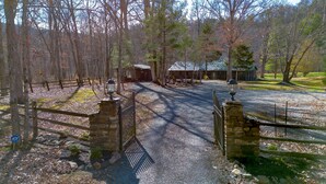 A gravel driveway leading to a stone gate with a metal fence, surrounded by trees and a building with a metal roof. - Riverfront country setting (Bath County)