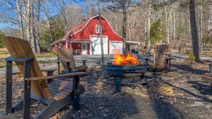 A red barn with a fire pit in the center, surrounded by wooden chairs and a table. - Riverfront country setting (Bath County)