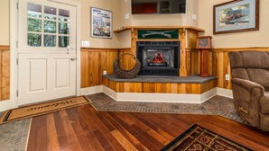 A cozy living room with a fireplace, wooden paneling, a comfortable armchair, and a door with glass panels. - Riverfront country setting (Bath County)