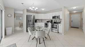 A modern kitchen with white cabinets, stainless steel appliances, and a glass dining table. - Disney Marvelous 4-bedroom house with a pool (Kissimmee)
