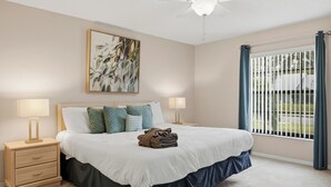 A bedroom with a bed, two bedside tables, a ceiling fan, a window with curtains, and a painting on the wall. - Disney Marvelous 4-bedroom house with a pool (Kissimmee)