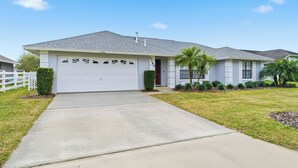 A single-story house with a white garage door, a red door, and a grey roof. - Disney Marvelous 4-bedroom house with a pool (Kissimmee)