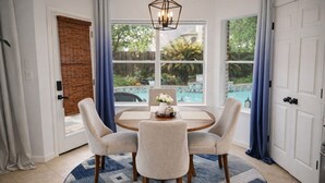 A dining area with a round table, four chairs, a vase with flowers, and a view of a swimming pool through large windows. - Luxurious 6-bedroom house with pool, grand piano and massage chair in Houston (Houston)