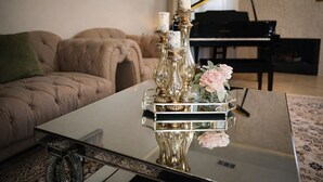 A living room with a tufted sofa, a glass coffee table with a decorative centerpiece, and a grand piano in the background. - Luxurious 6-bedroom house with pool, grand piano and massage chair in Houston (Houston)