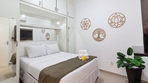 Une chambre d’hôtel bien rangée, avec un lit, une table de chevet, une plante en pot et des œuvres d’art décoratives accrochées au mur.