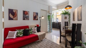 Un salon moderne avec un canapé rouge, un coin repas comprenant une table et des chaises, et des  œuvres d’art accrochées aux murs.