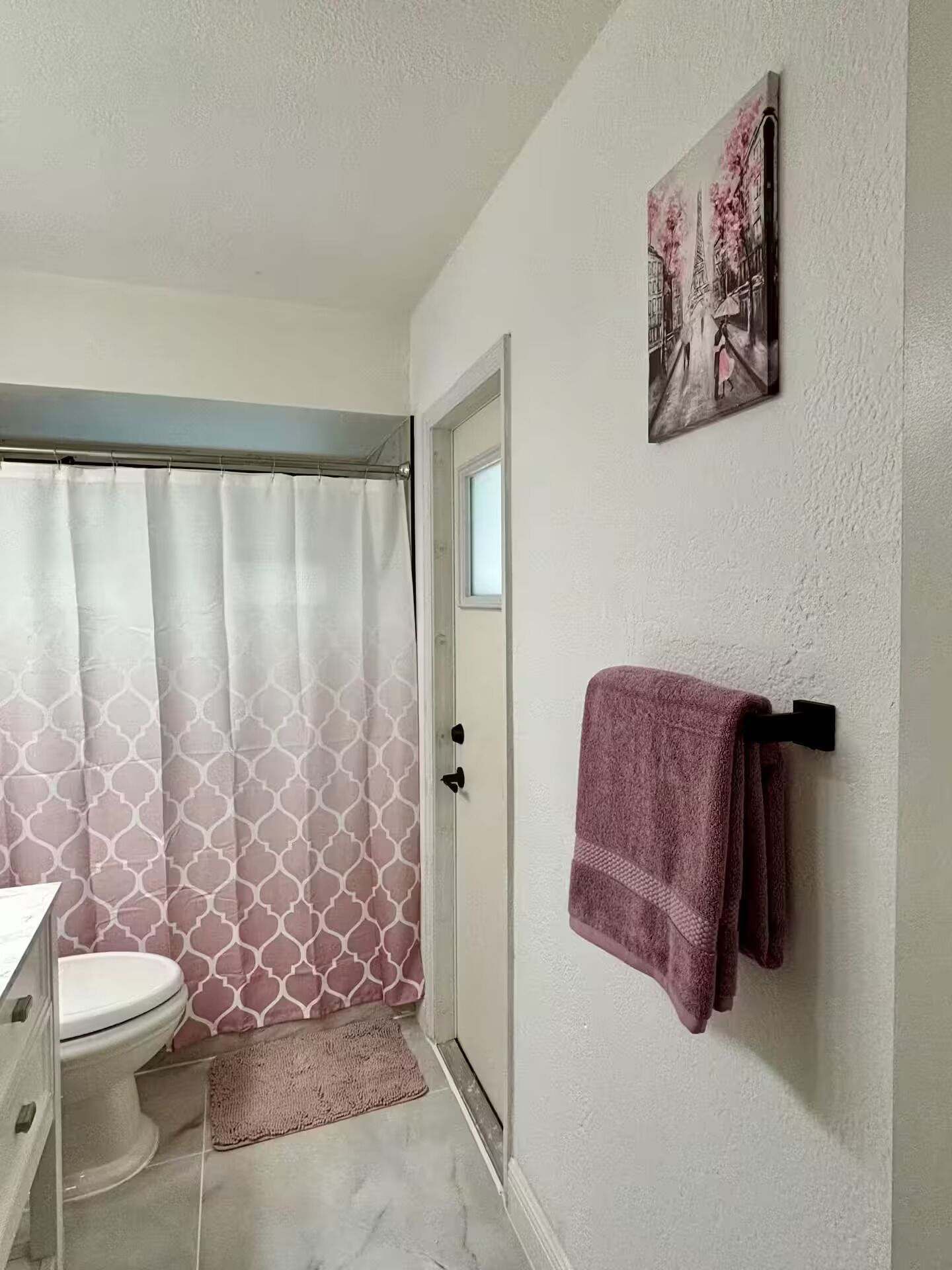 A bathroom with a toilet, shower curtain, towel rack, and a door.