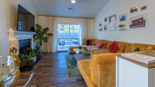 A living room with a sofa, a coffee table, and a fireplace. There are potted plants and a large window. - Stylish Durham Retreat • 3BR, Private Backyard • Near NCCU, Duke & Downtown (Durham)