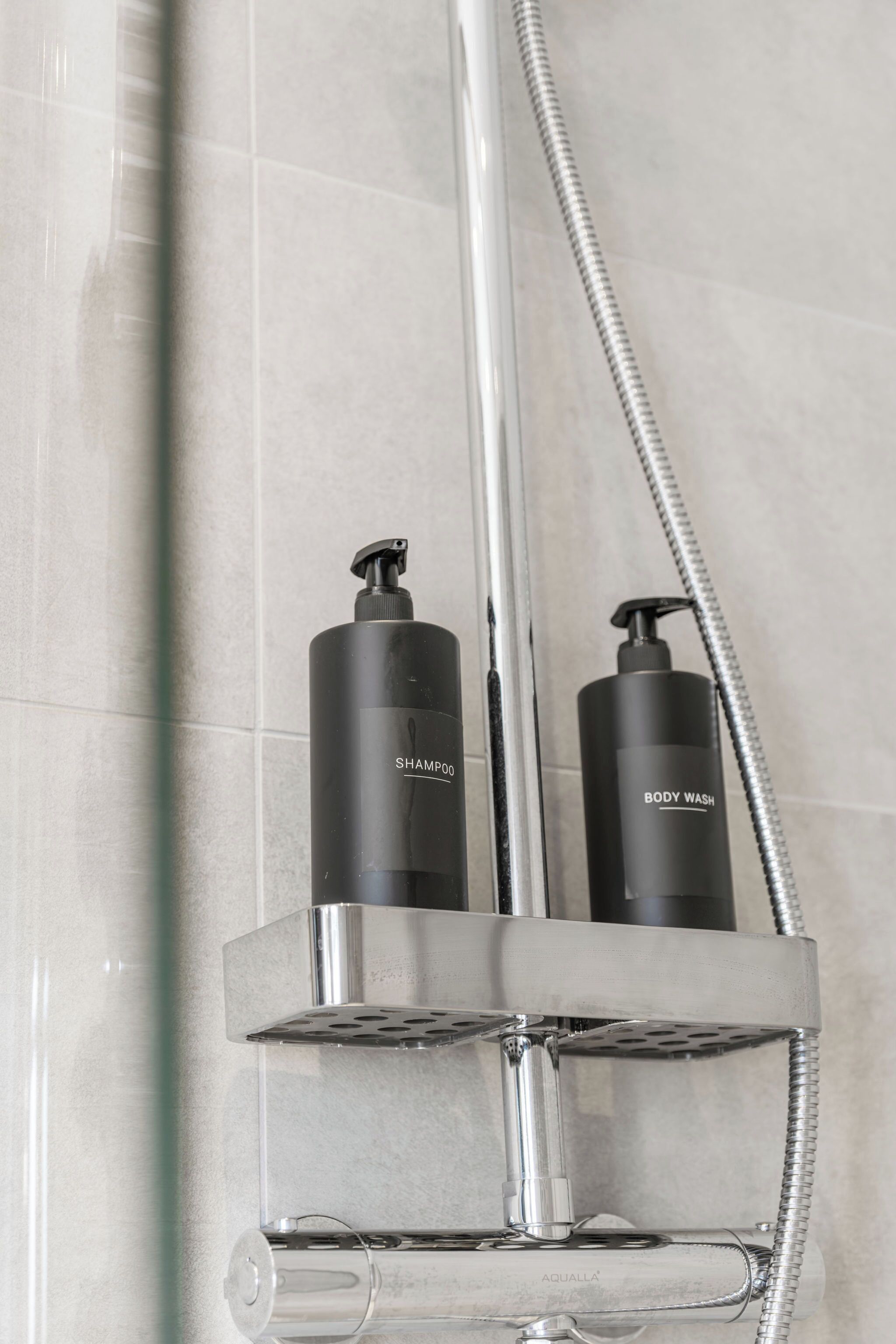 Ein Badezimmer mit Duschkopf aus Chrom, zwei schwarzen Shampooflaschen und einer Flasche Duschgel.