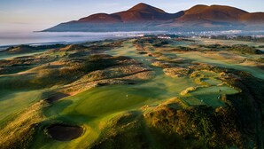 Un campo de golf con terreno ondulado y búnkeres, rodeado de montañas y vistas al mar.