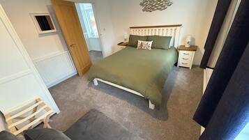 Een slaapkamer met een bed, nachtkastje, dressoir, raam en deur.