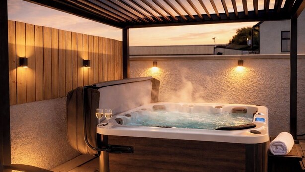 Un jacuzzi con dos copas de vino, una toalla y una pérgola de madera.
