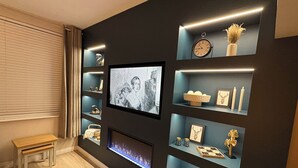 Una sala de estar moderna con un televisor de pantalla plana montado en la pared, rodeada de estantes con objetos decorativos y libros.
