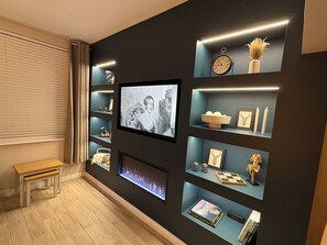 Ein modernes Wohnzimmer mit einem flachbildfernseher an der Wand, umgeben von Regalen mit Dekoration und Büchern.