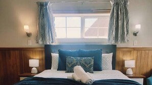 Una cama bien hecha con ropa de cama estampada, dos lámparas de noche y un ventanal con cortinas.