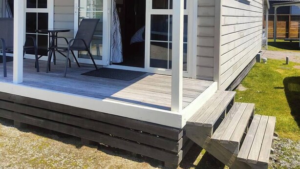 Una casa de un piso con porche cubierto, puerta corrediza de vidrio y un pequeño espacio exterior con dos sillas y una mesa.