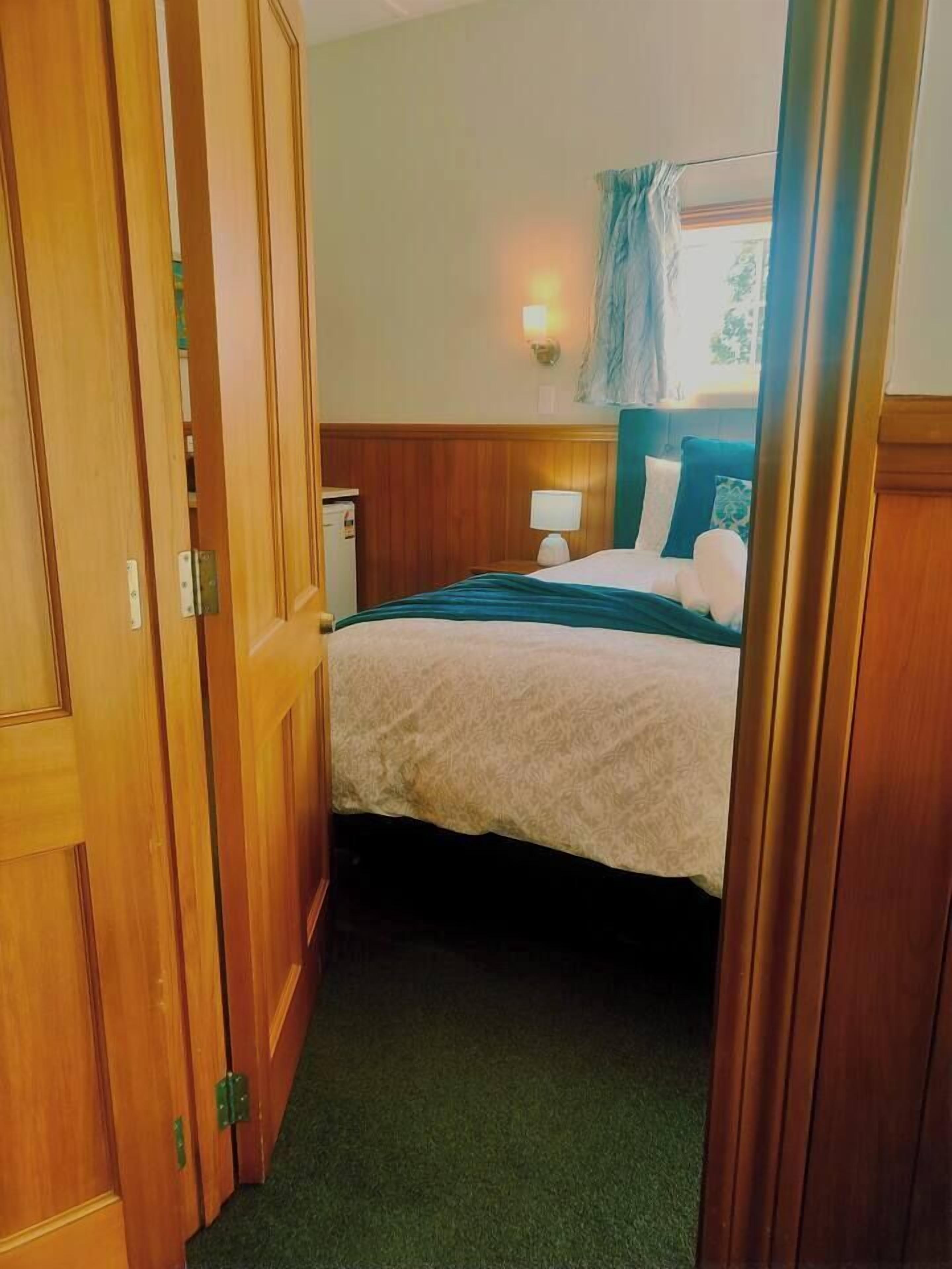 Et hotelværelse med en seng, et natbord, en lampe og et vindue med gardiner.