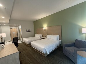 Habitación de hotel con dos camas, un escritorio, una silla, un sofá y una lámpara fijada a la pared.