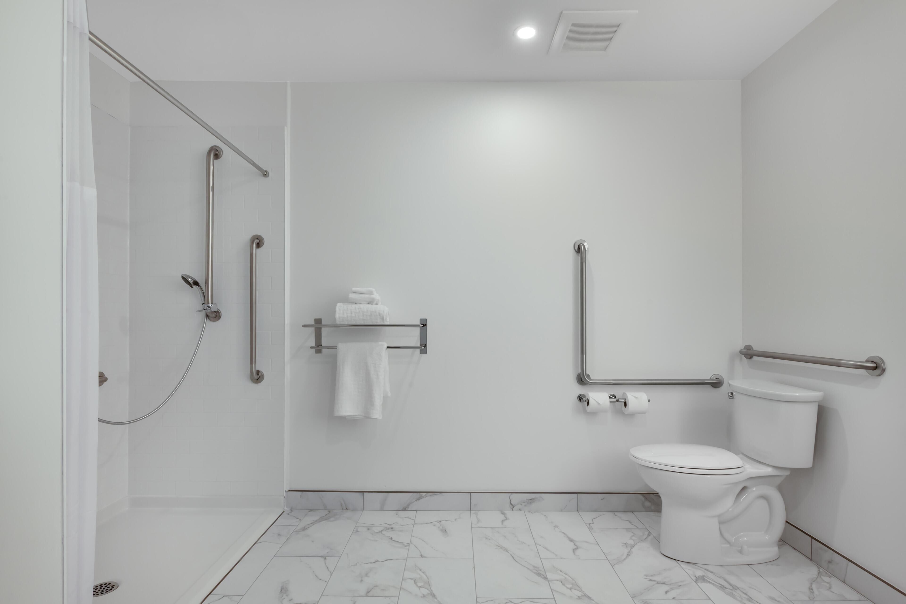 A modern bathroom with a shower, toilet, and grab bars.