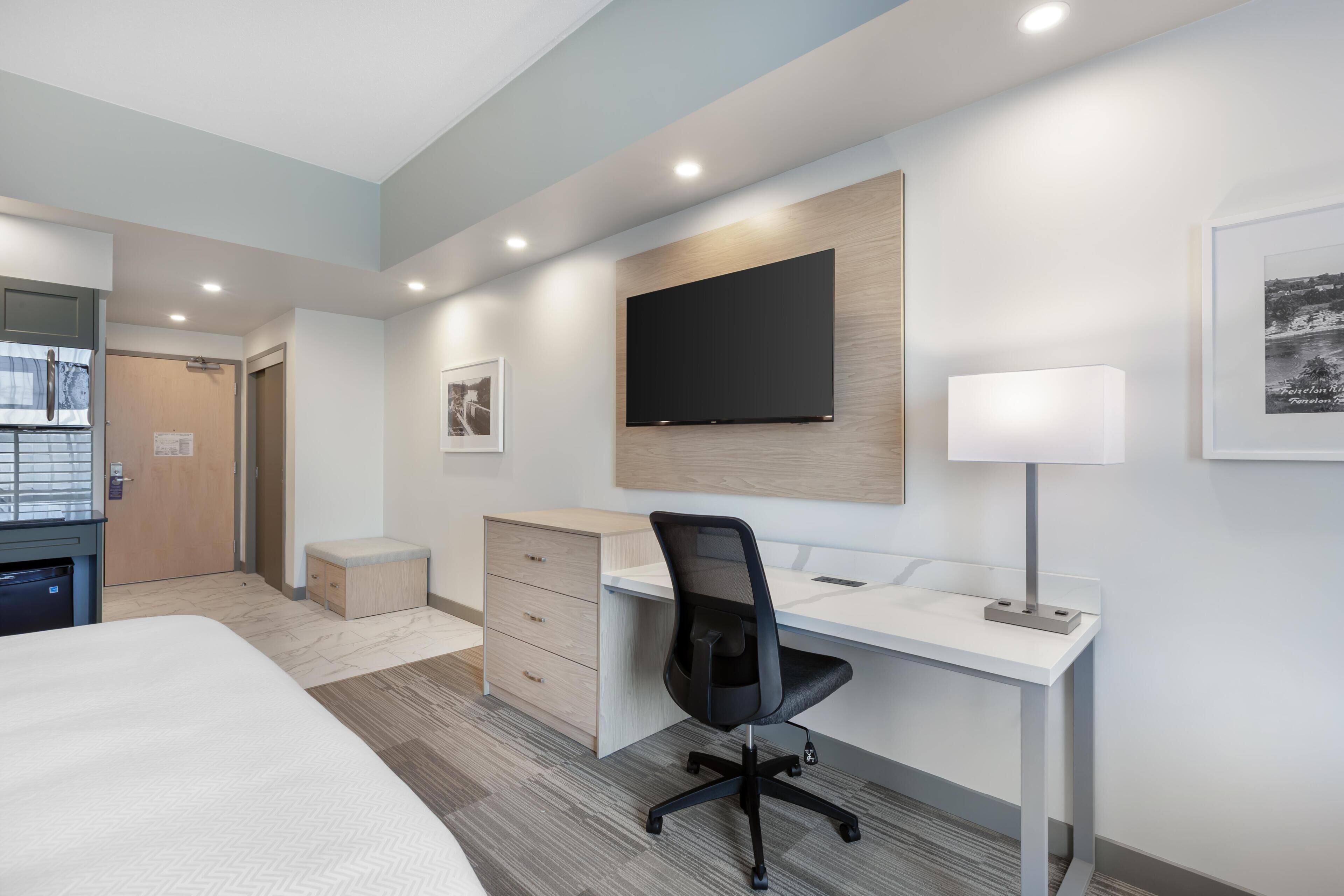 Ein modernes Hotelzimmer mit Bett, Schreibtisch, Stuhl, Fernseher und Kunstwerken an den Wänden.