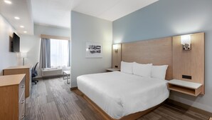 Une chambre d’hôtel avec un grand lit, un bureau avec une chaise, un téléviseur fixé au mur et une fenêtre avec des rideaux.