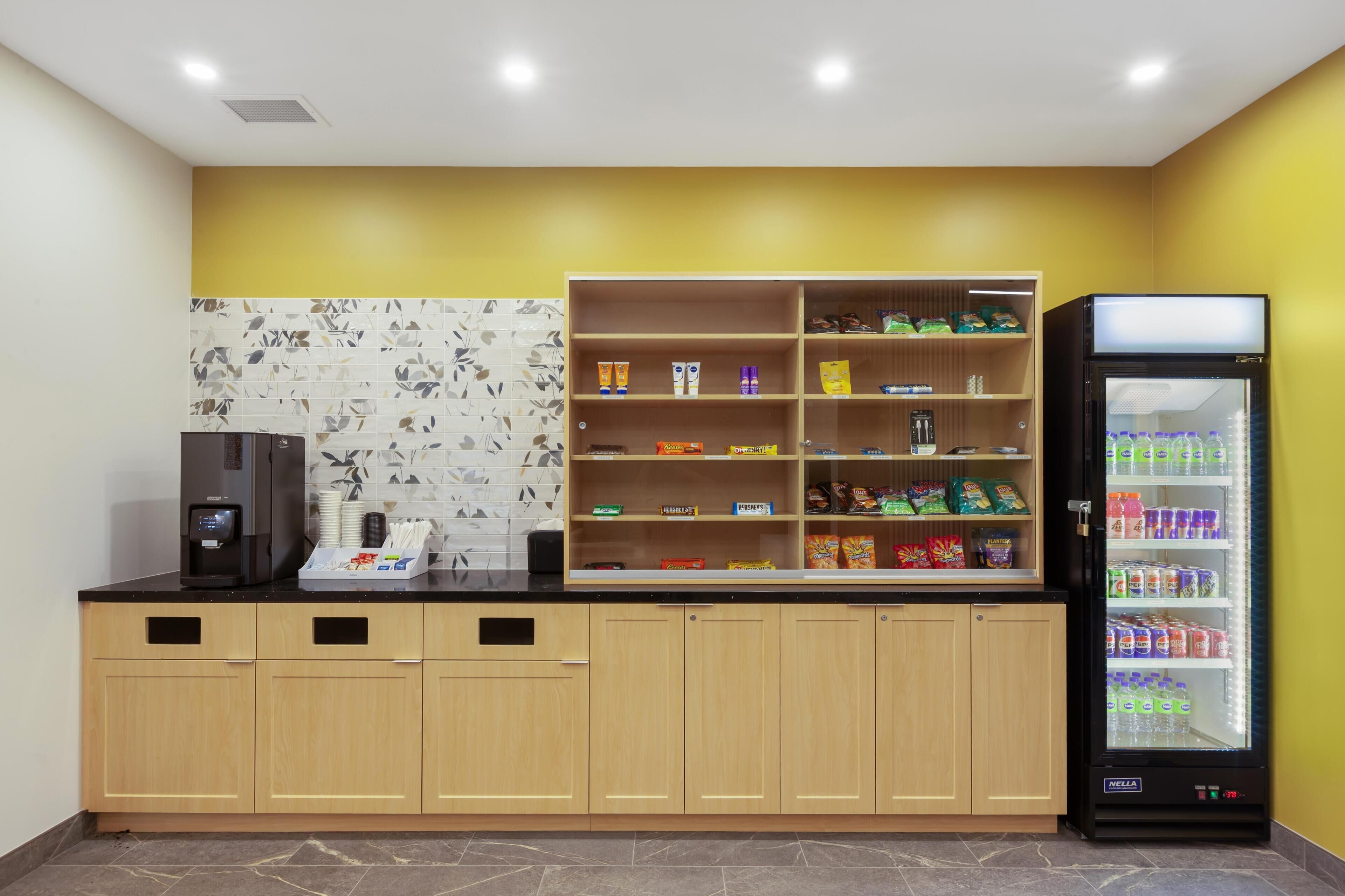 Una kitchenette con una máquina de café, un dispensador de bebidas y un refrigerador lleno de bebidas.