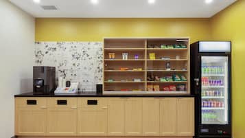 Una kitchenette con una máquina de café, un dispensador de bebidas y un refrigerador lleno de bebidas.