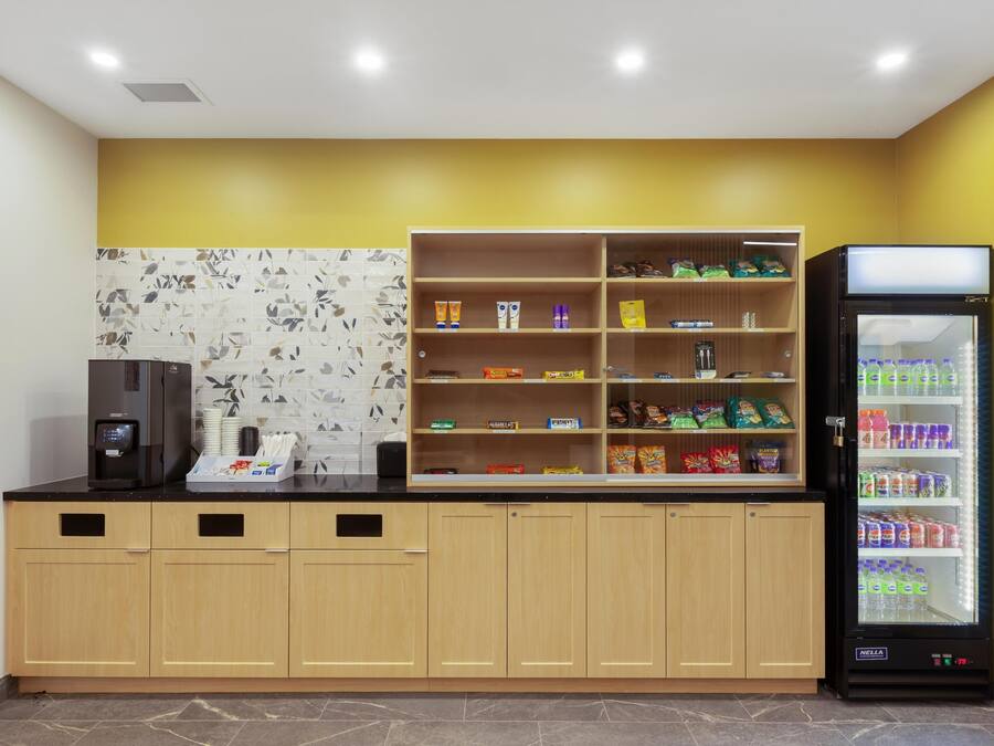Una kitchenette con una máquina de café, un dispensador de bebidas y un refrigerador lleno de bebidas.